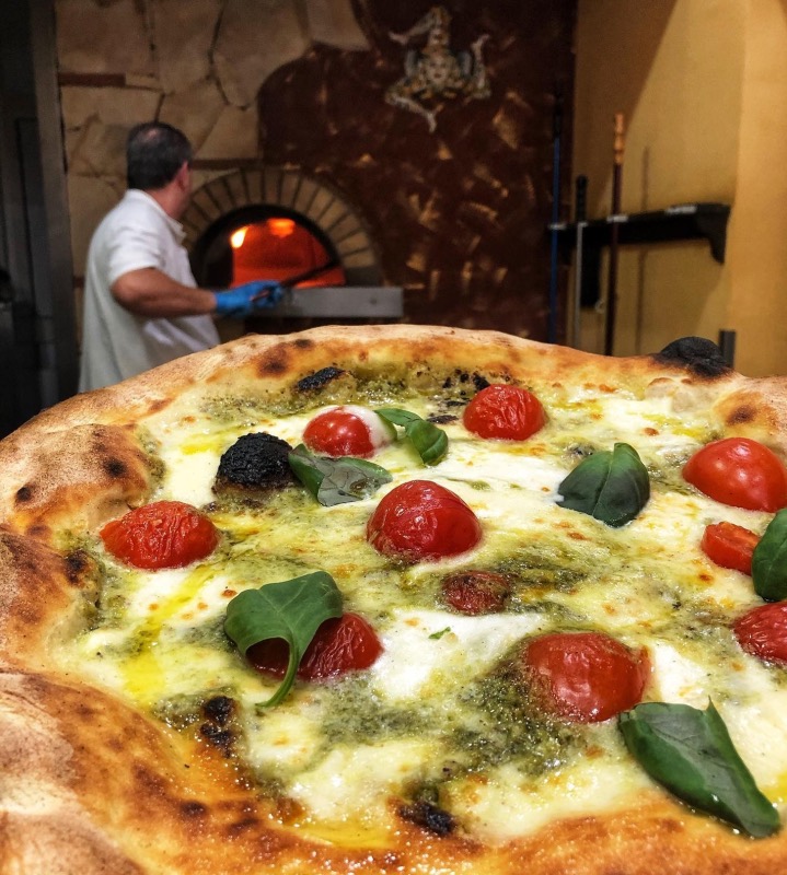 Una pizza al pesto appena sfornata davanti al forno a legna